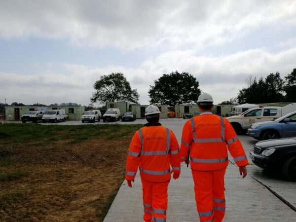 two surveyors in orange walking away from camera on large construction site