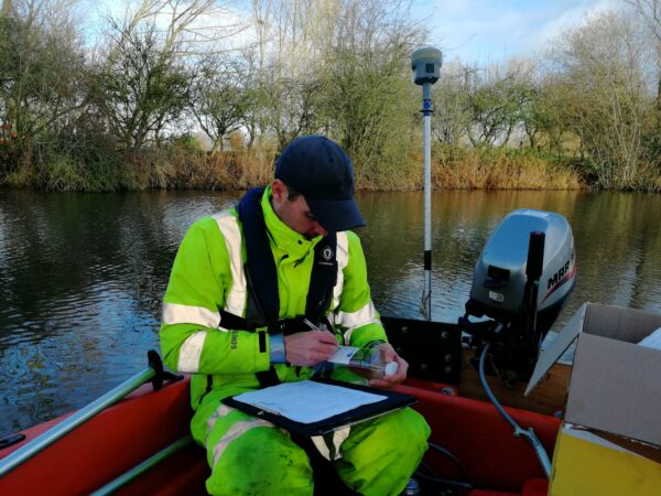 surveyor in small boat in orange high vis writing on water sample container